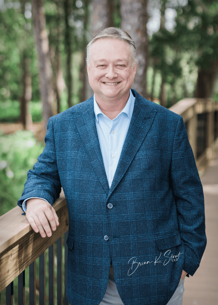 Business professional smiling in a park with trees in the background.